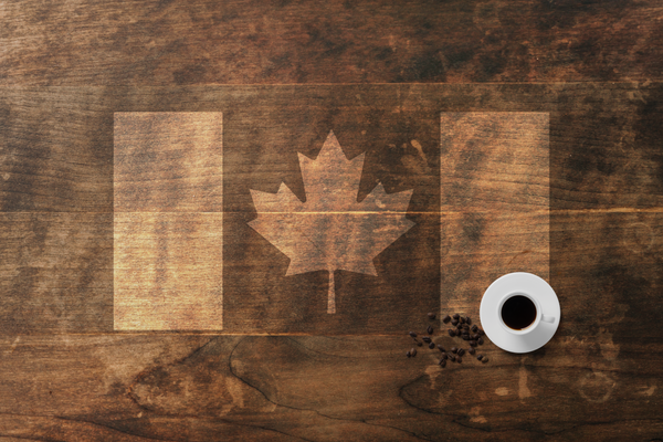 The Canadian flag over a wooden table with a cup of coffee and coffee beans off to the side.