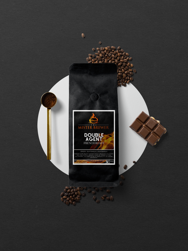 An aerial photo of a bag of our Double Agent roast alongside a gold coffee scoop and a dark and nutty piece of chocolate.